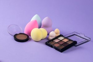 Several Beauty Blenders and What Appears to be an Eyeshadow Palette and Concealer Placed on a Purple Surface