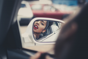 A Woman Applying Lipstick In A Rearview Mirror